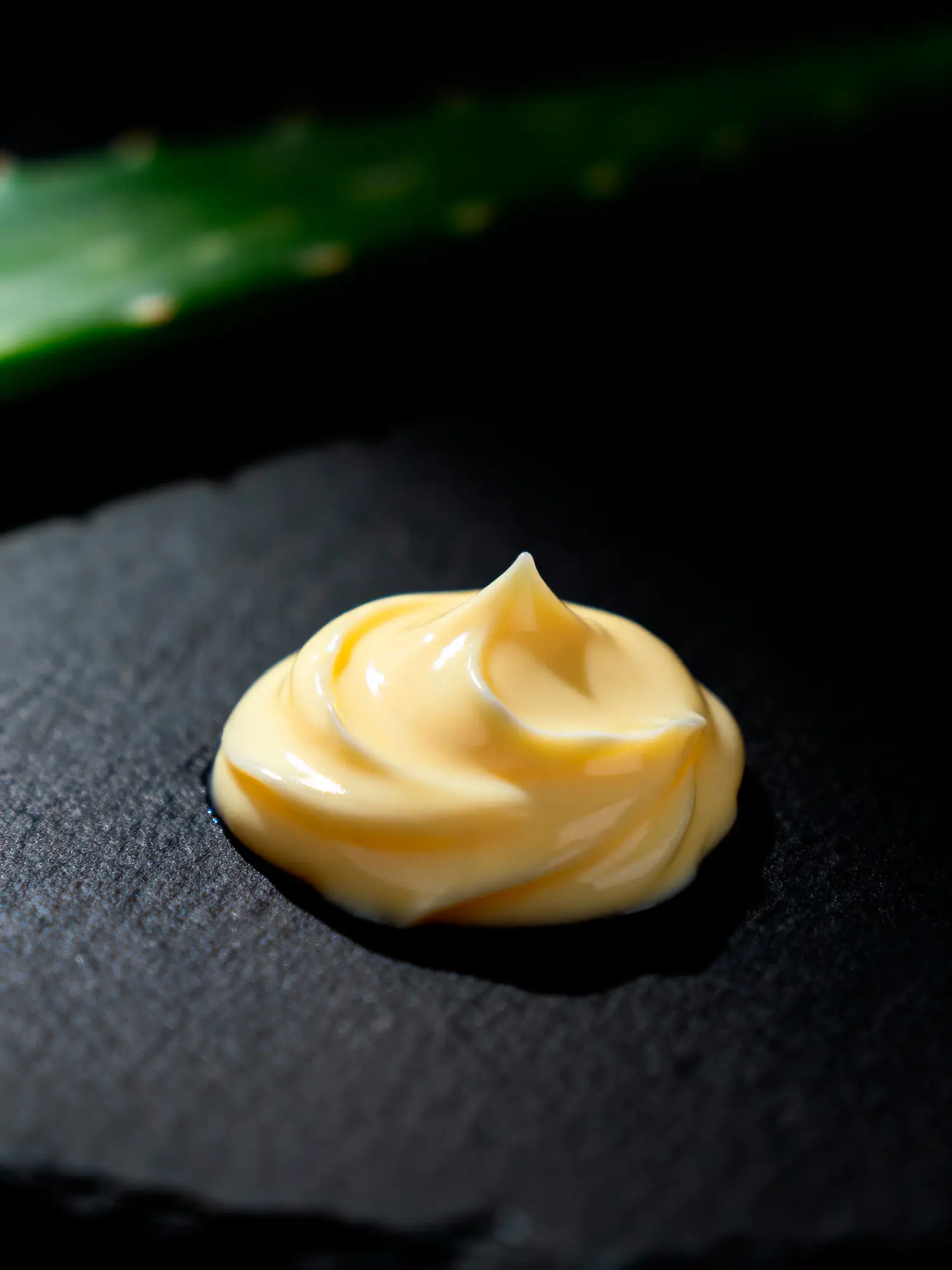 Swirl of amber retinoid night cream on dark slate beside an aloe leaf